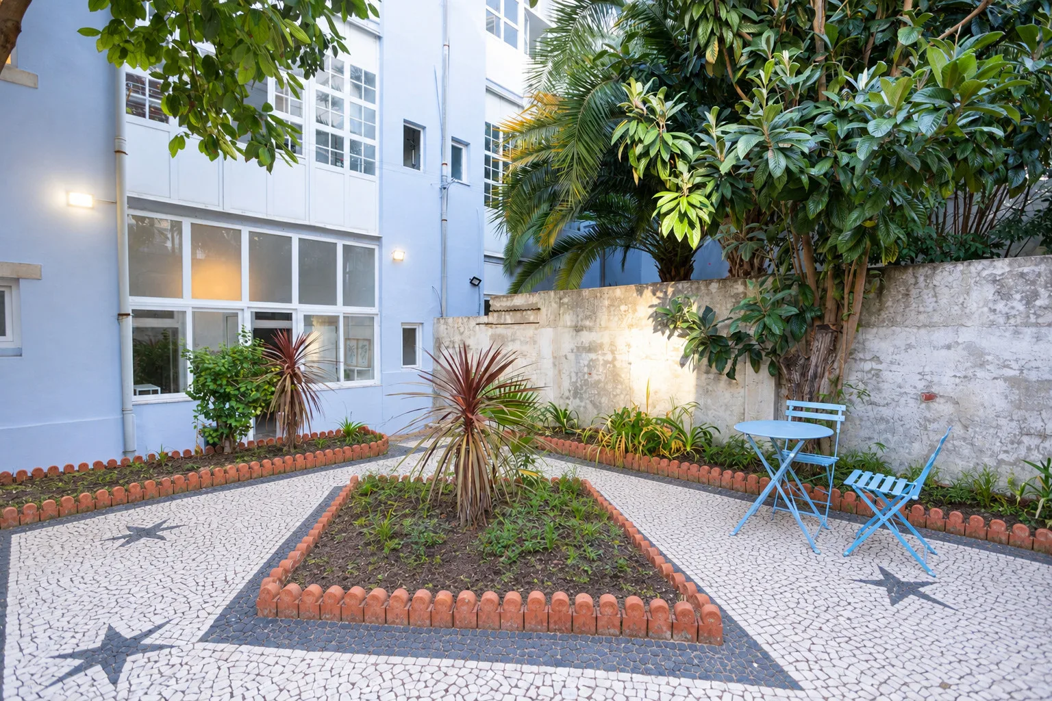 A courtyard garden with paved paths, leafy trees, and blue outdoor seating.