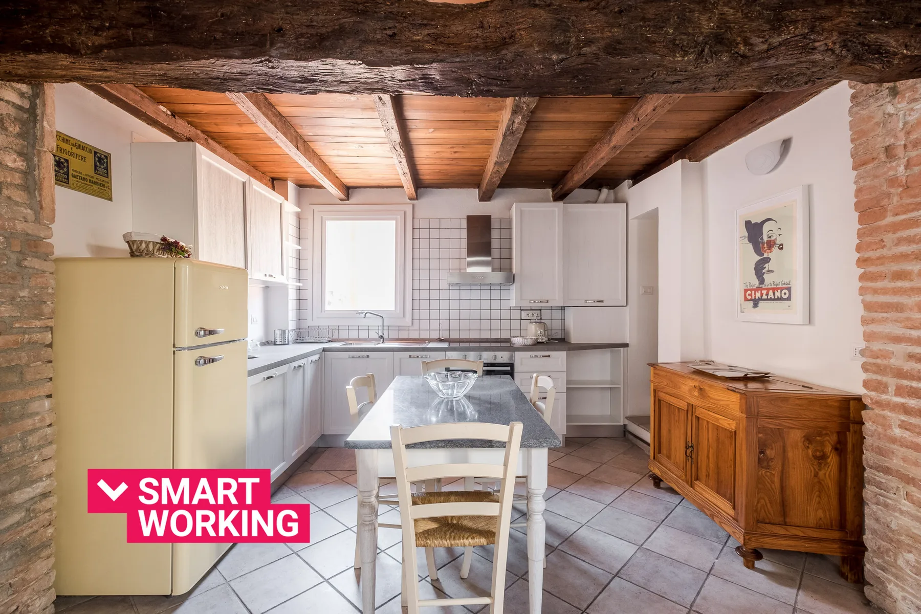 Una cocina luminosa con gabinetes blancos, un refrigerador y una mesa de comedor.