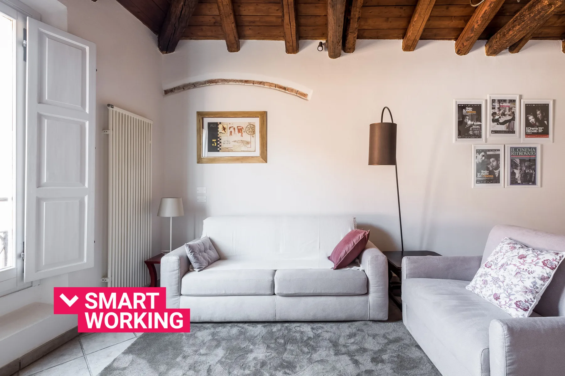 A bright living room with white seating and exposed wooden ceiling beams.