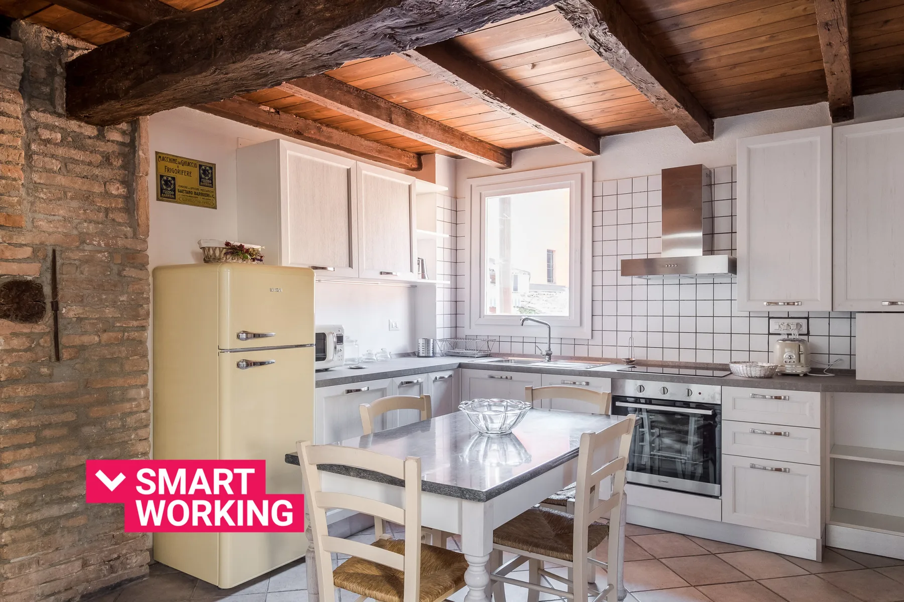 A bright kitchen with white cabinets, a dining table, and exposed wooden ceiling beams.