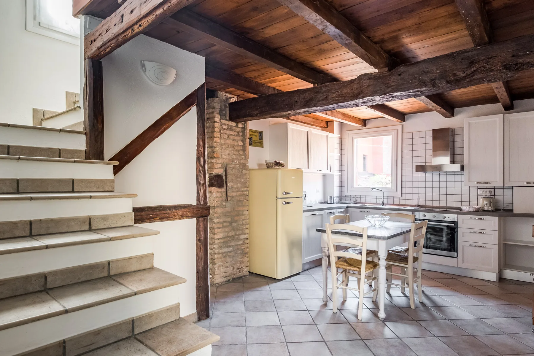 Cocina y comedor bajo vigas de madera vistas, con una escalera a un lado.