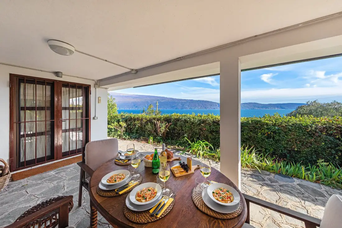 A covered outdoor dining area overlooks a garden and the water.