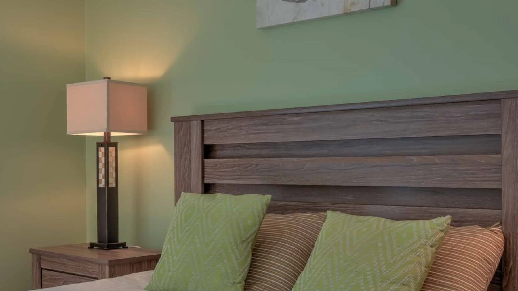Un dormitorio con cabecero de madera, almohadas y una lámpara de mesita.