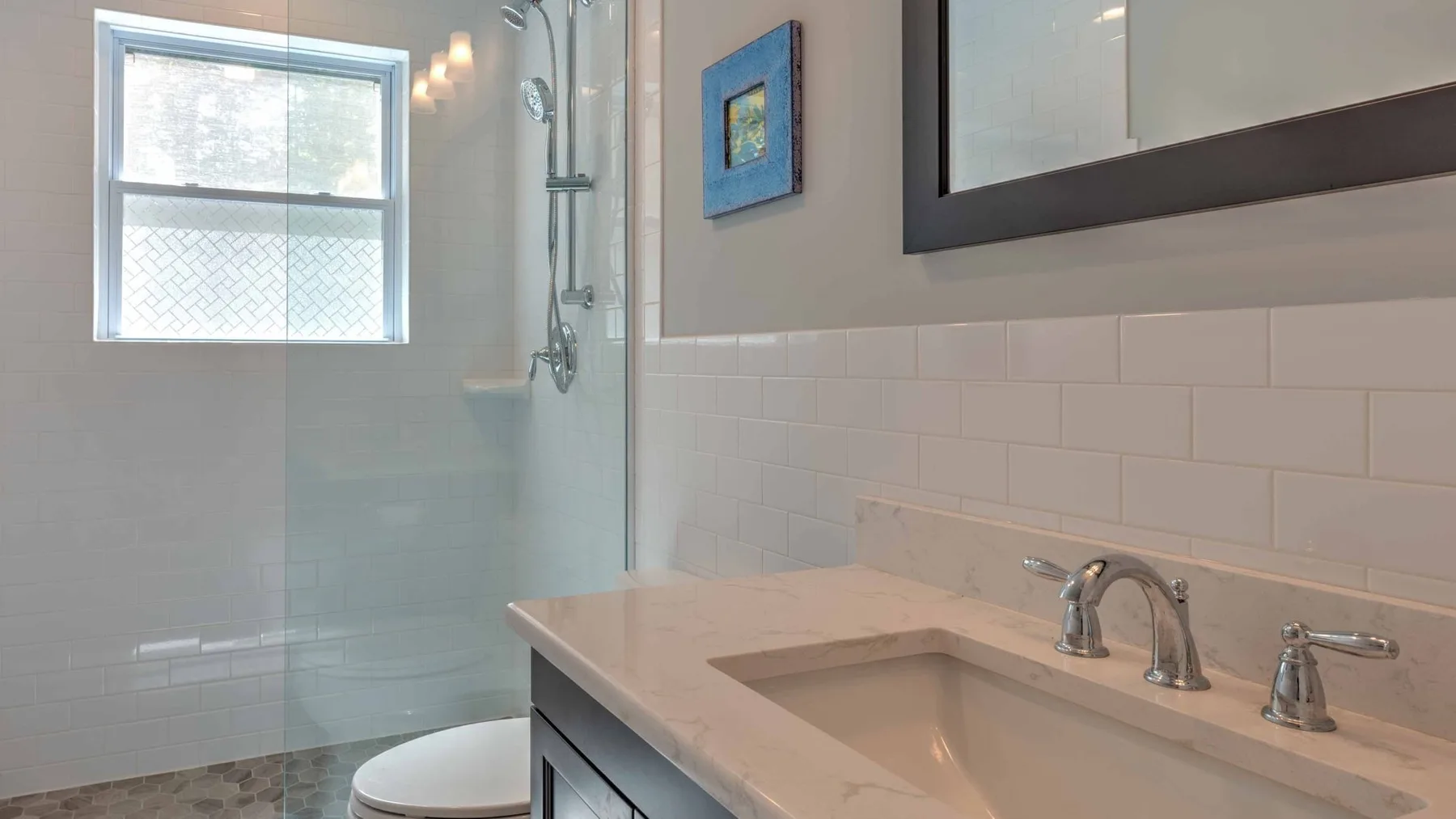 Un baño con ducha de vidrio, una ventana y un lavabo con mueble.