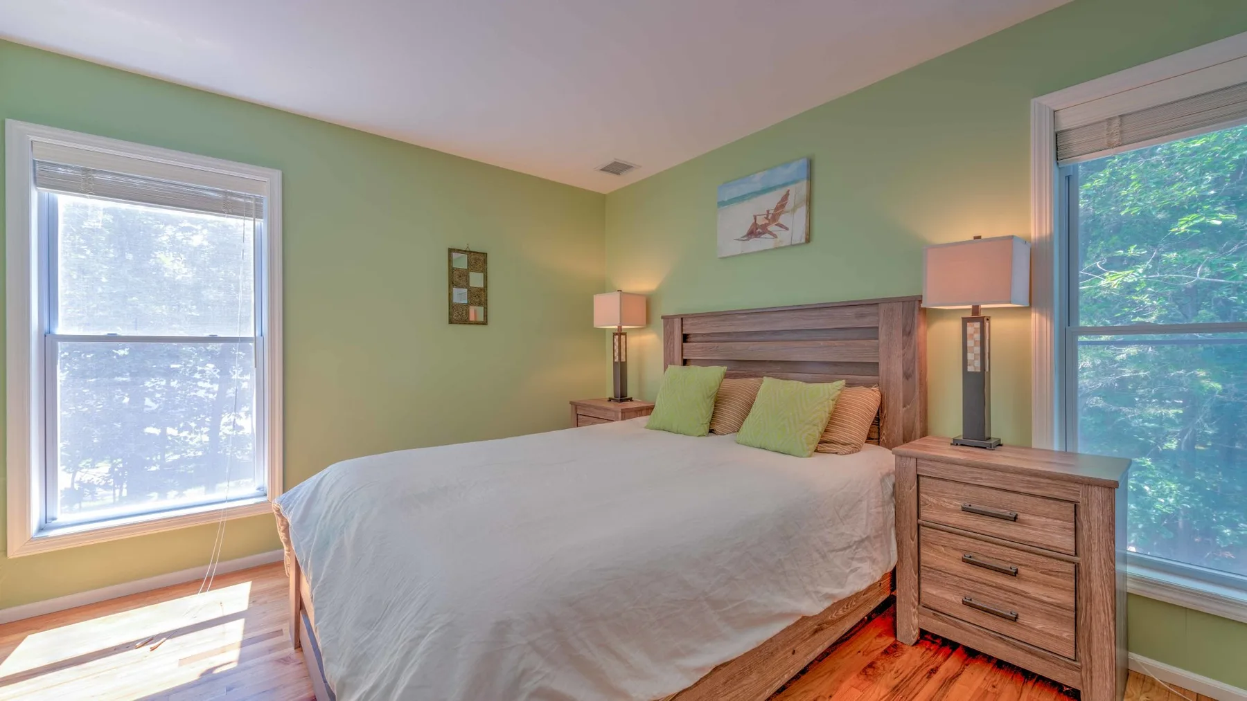 Un dormitorio con una cama, paredes verdes y ventanas a ambos lados.