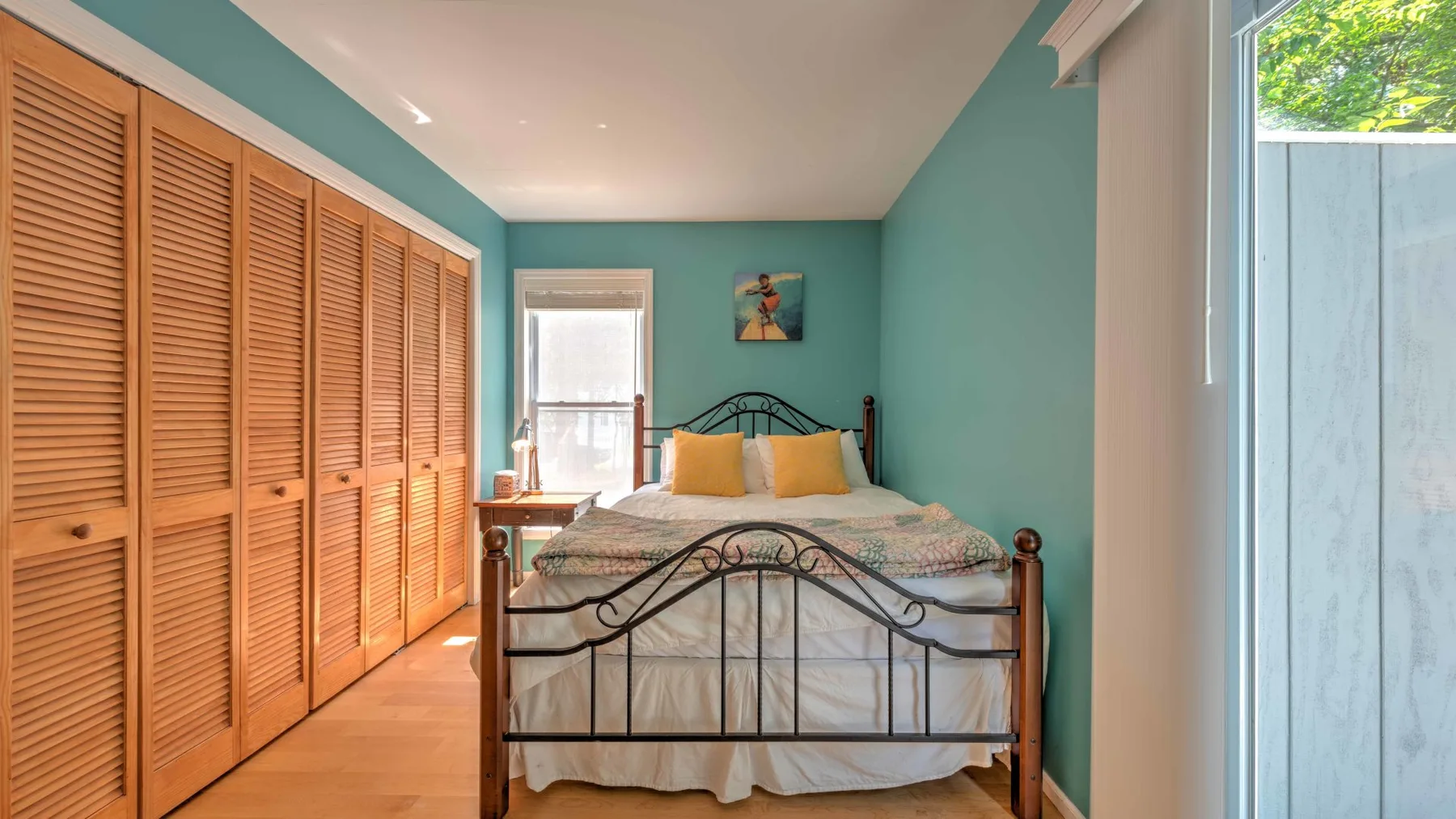 Un dormitorio con una cama, armarios de madera con persianas y paredes verde azulado.