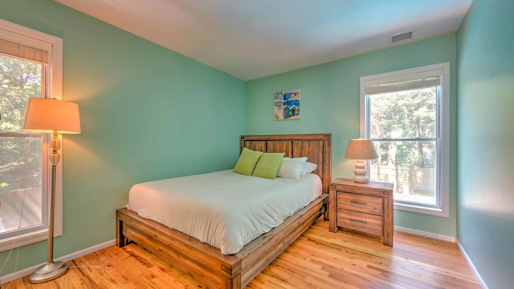 Un dormitorio con una cama de madera, ropa de cama blanca y paredes verdes.