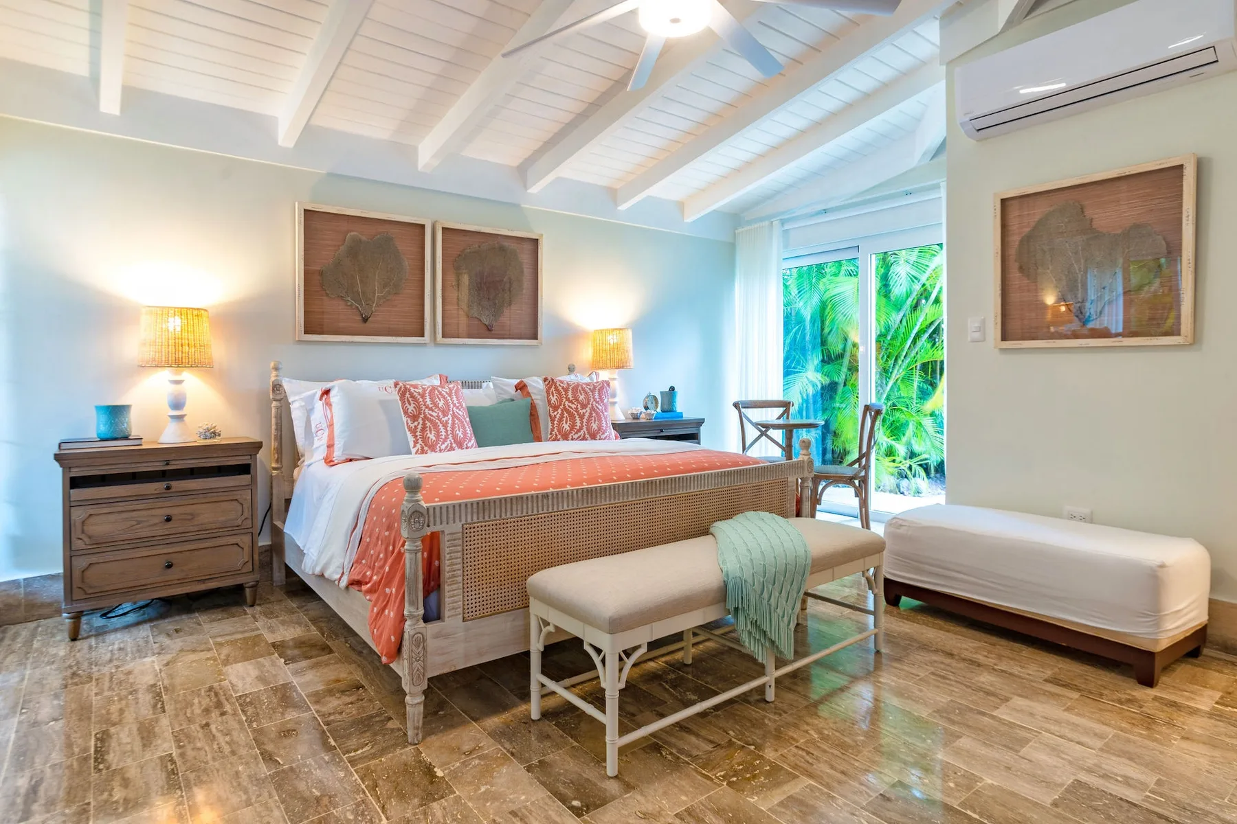 A bright bedroom with a large bed, a bench, and glass doors opening onto greenery.