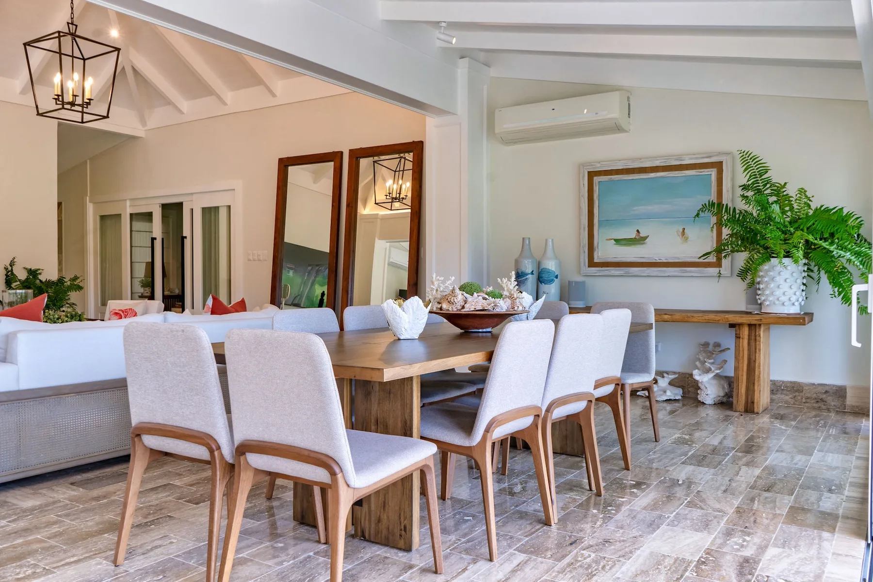 A bright dining area has a wooden table, upholstered seating, and a potted plant.