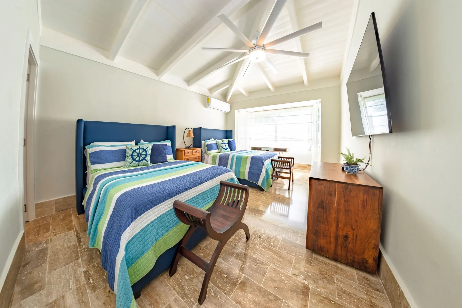 A bright bedroom with blue beds, colorful bedding, and a ceiling fan.