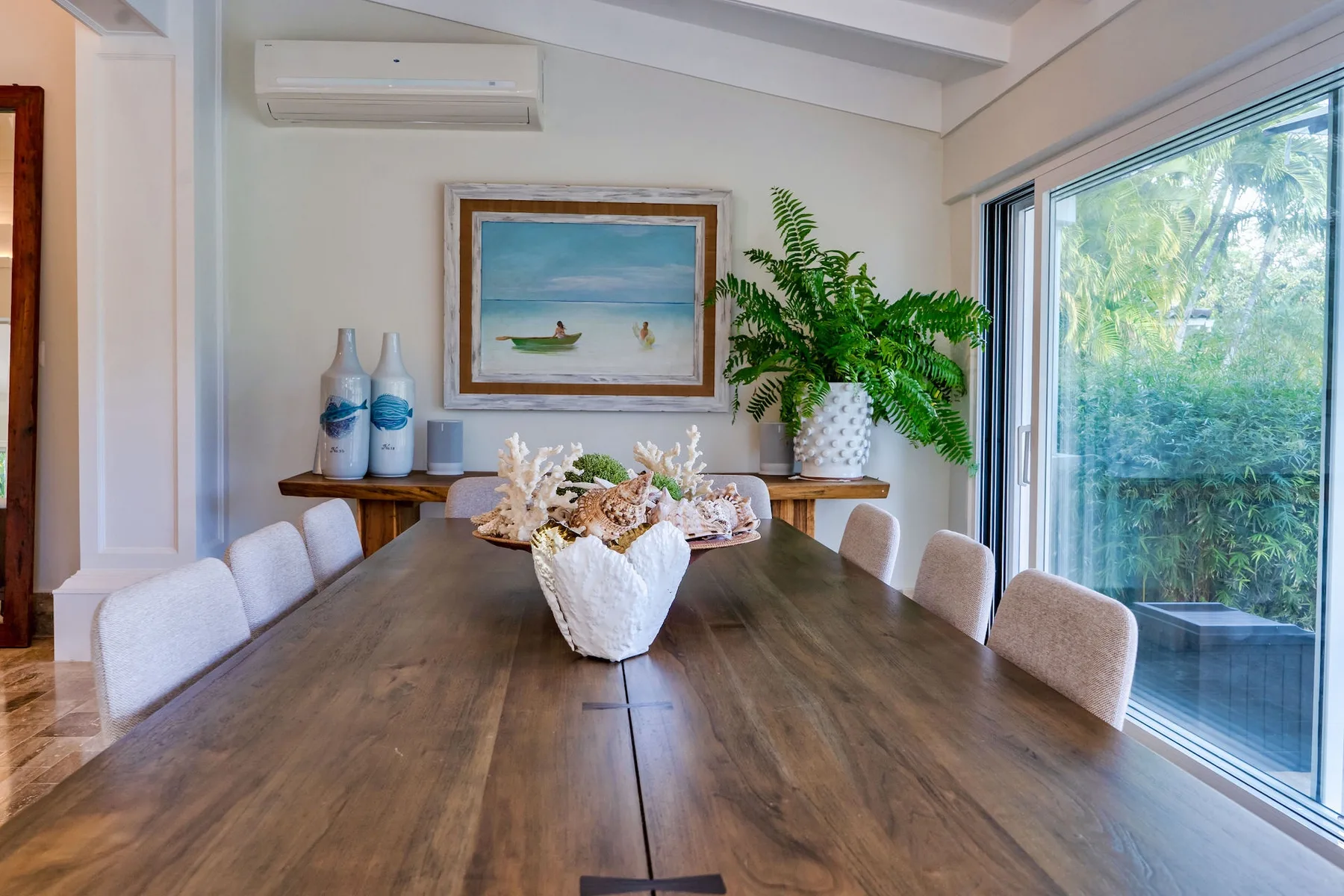 A dining room with a long wooden table, upholstered seating, and large windows.