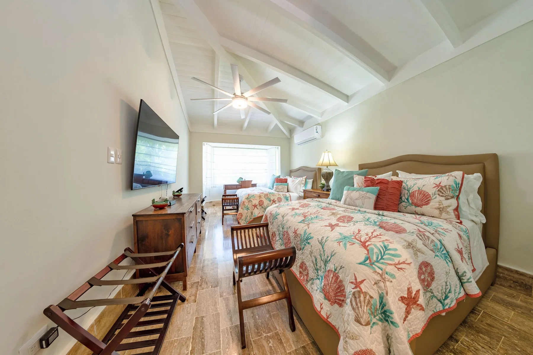 A bedroom with a large bed, patterned bedding, and a television mounted on the wall.