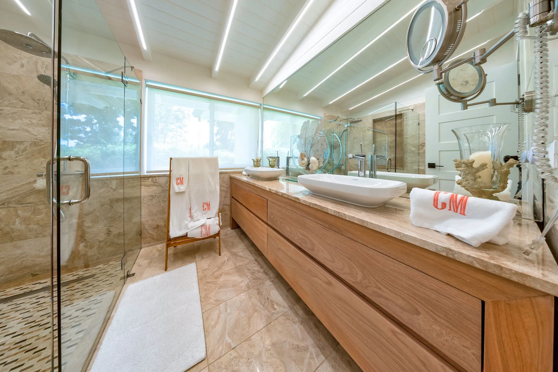 A bright bathroom with a long vanity, vessel sinks, and a glass shower.