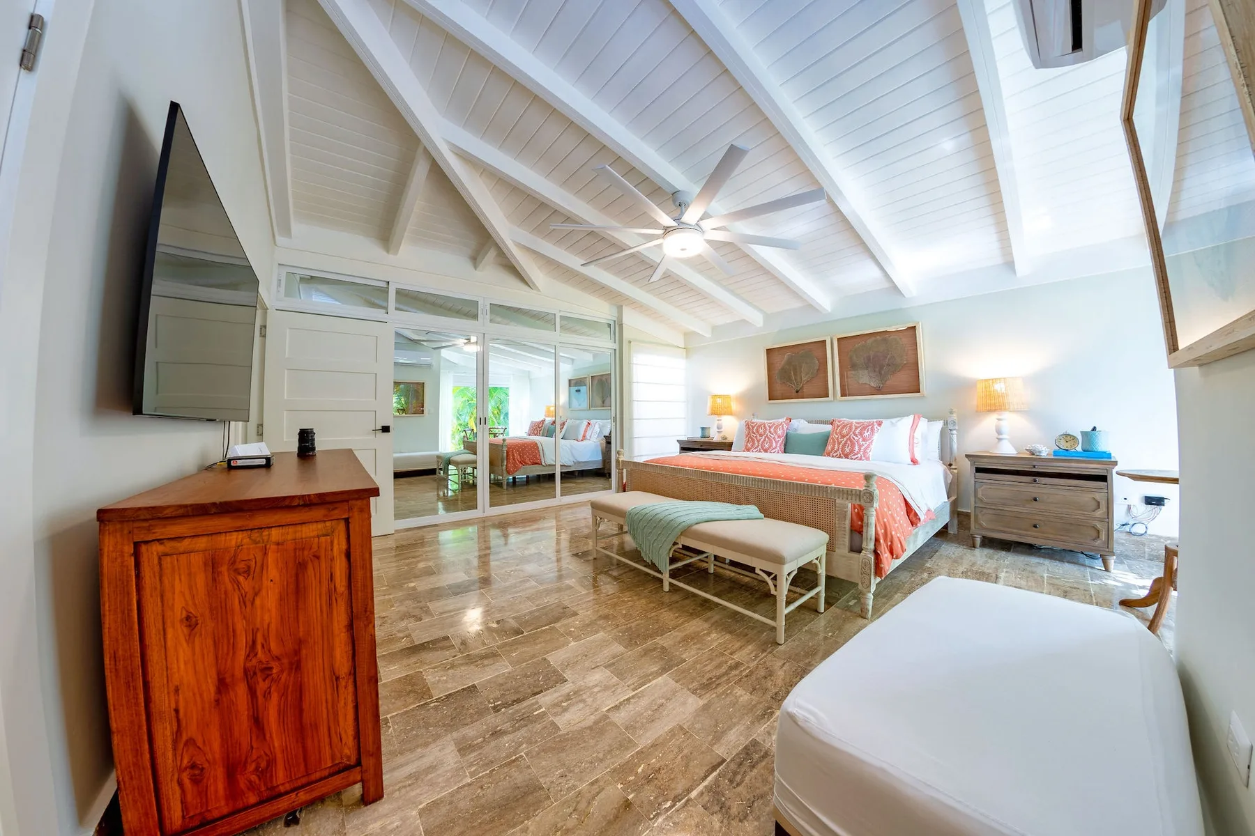 A bright bedroom with a bed, a sitting area, and a high beamed ceiling.
