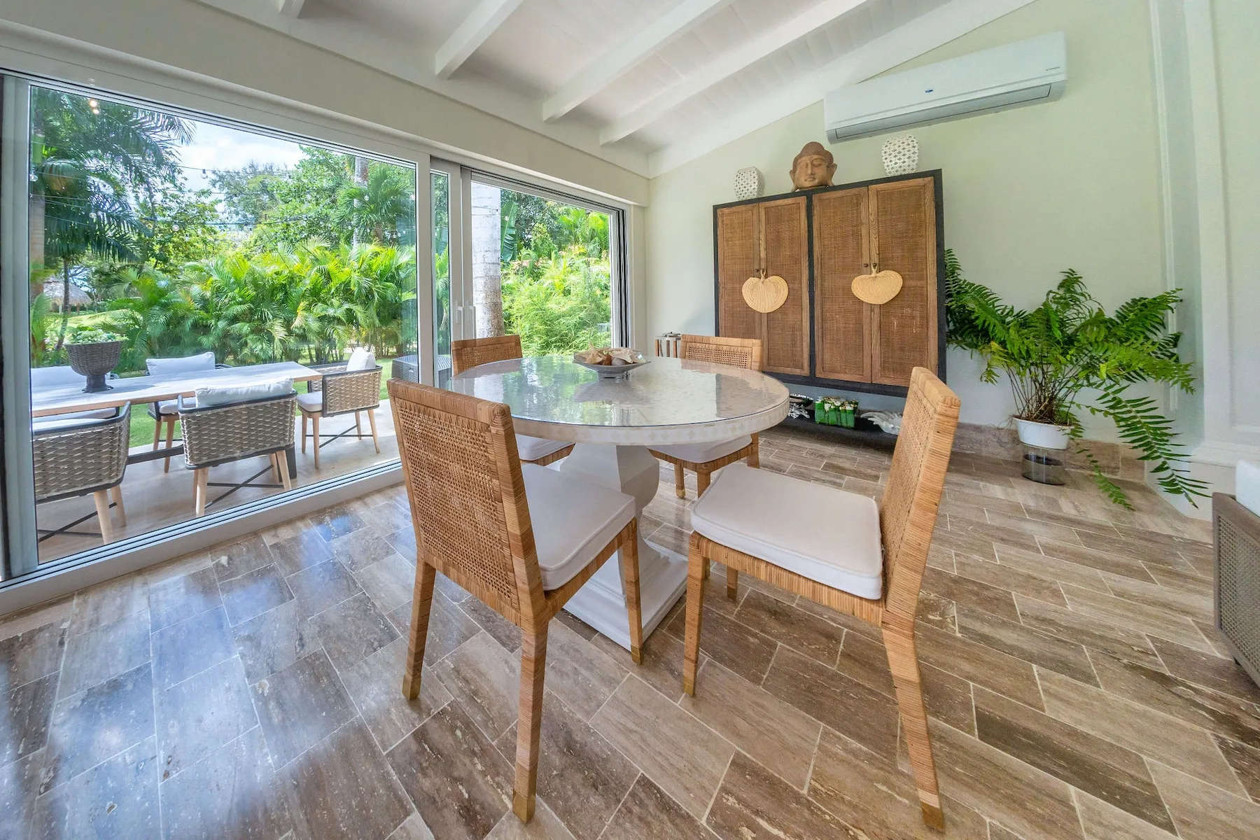 A dining area with a round table and chairs beside large windows overlooking greenery.