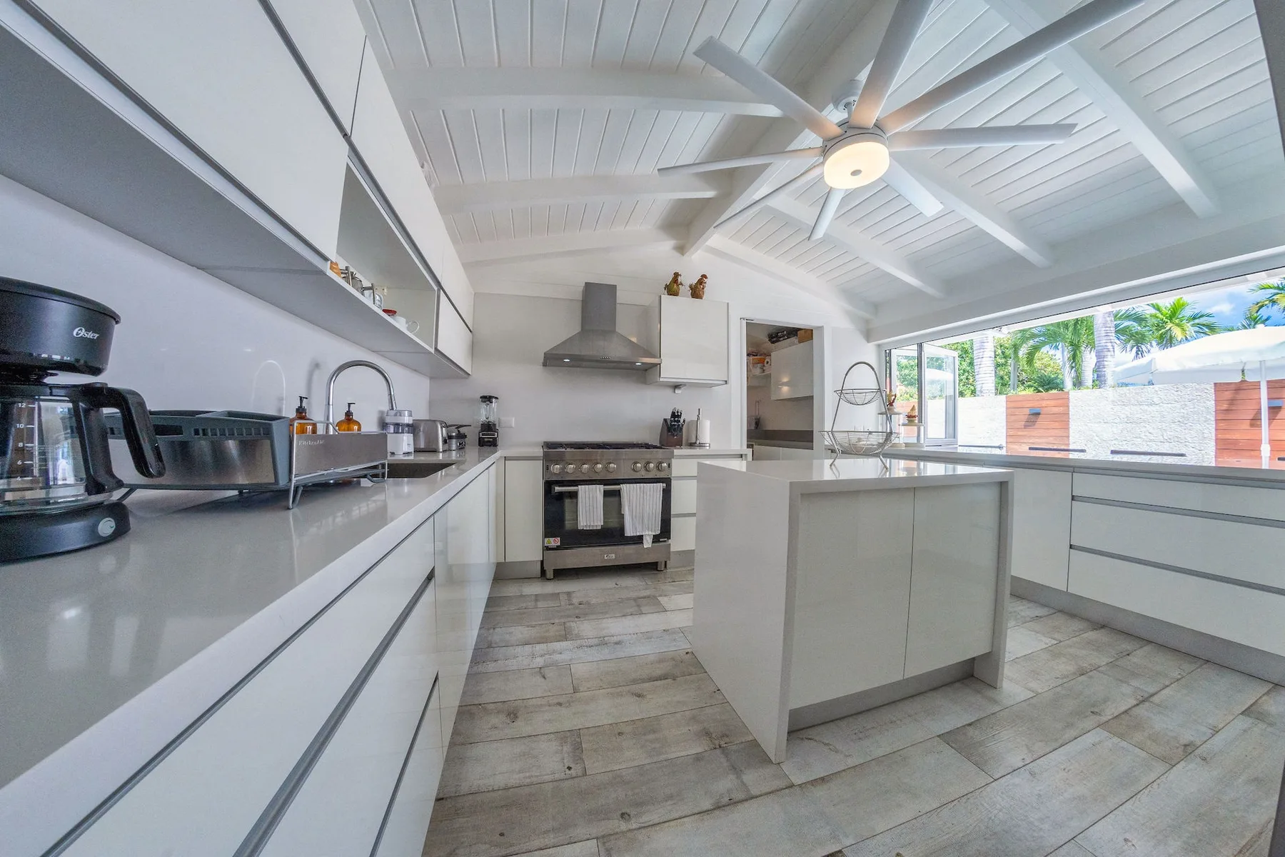 A bright kitchen with white cabinetry, a central island, and a large ceiling fan.