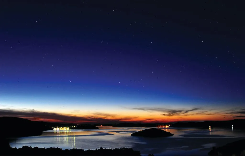 Un paisaje acuático al atardecer, con una orilla oscura bajo un cielo estrellado.