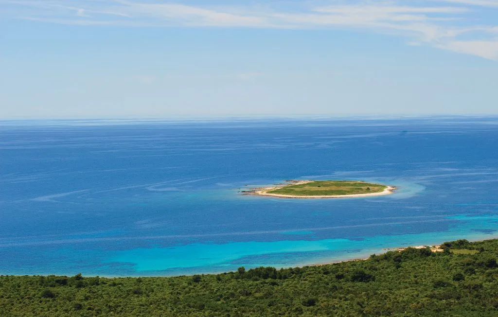 Una pequeña isla verde se encuentra en el océano azul, más allá de la costa.