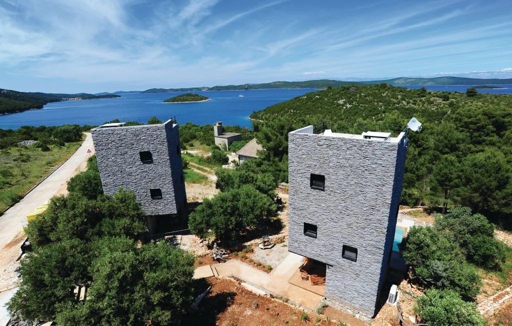 Dos edificios modernos se alzan entre árboles sobre una bahía azul.