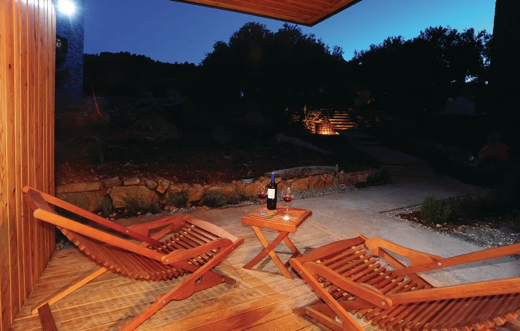 Un patio exterior de madera con tumbonas reclinables y una mesa pequeña al anochecer.