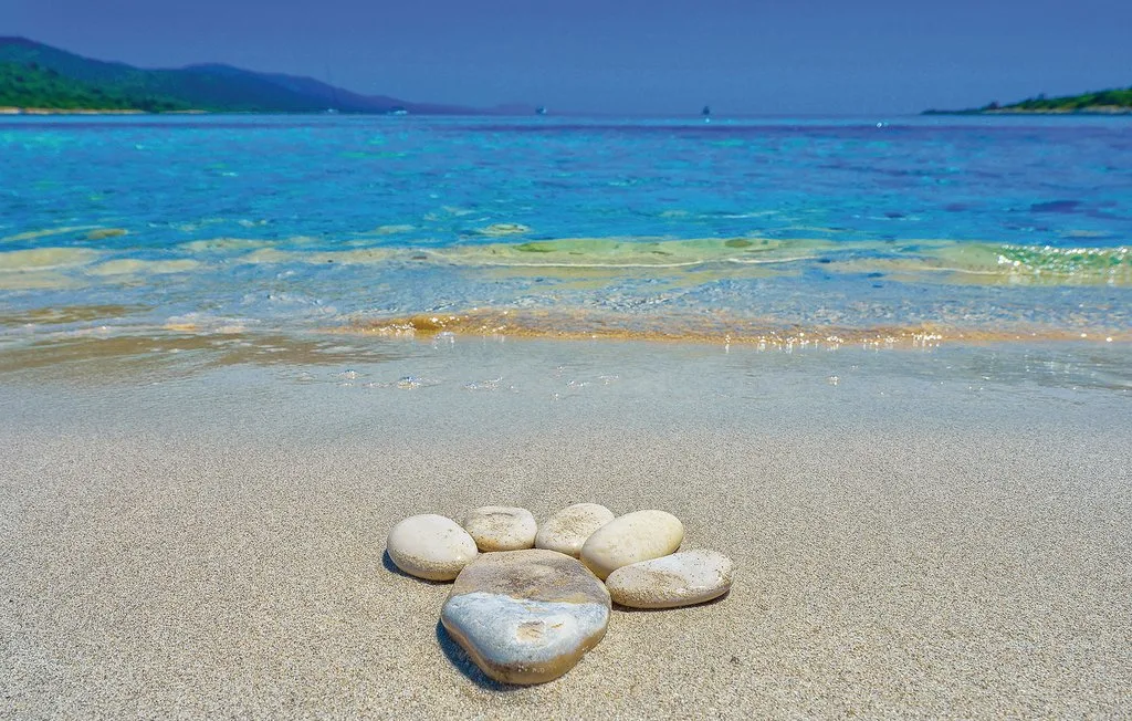 Una playa de arena con piedras lisas dispuestas junto al agua turquesa.