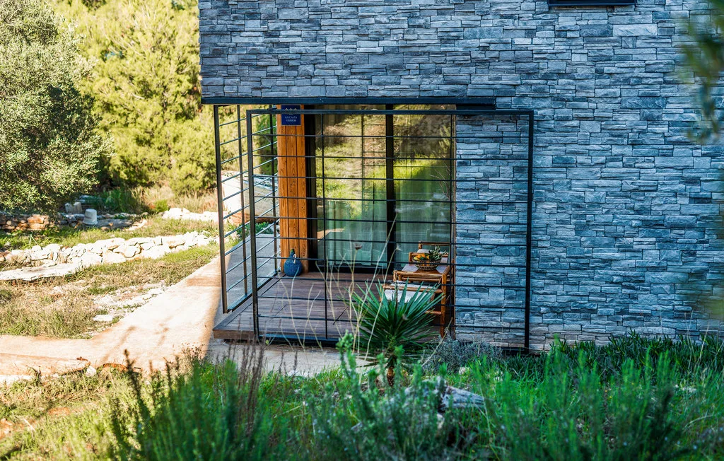 Un edificio revestido de piedra tiene una entrada acristalada junto a un camino soleado.