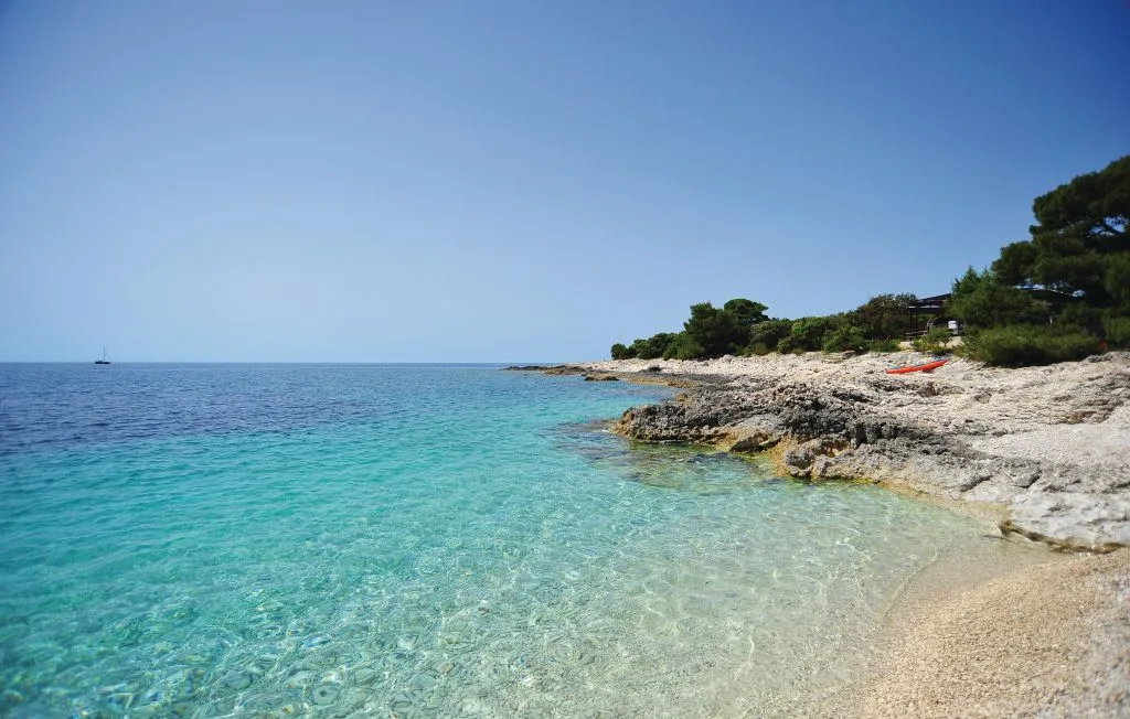 El mar turquesa y transparente llega a una costa rocosa con una pequeña playa de arena.