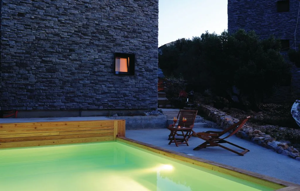 Una piscina exterior junto a edificios revestidos de piedra y asientos de patio al anochecer.