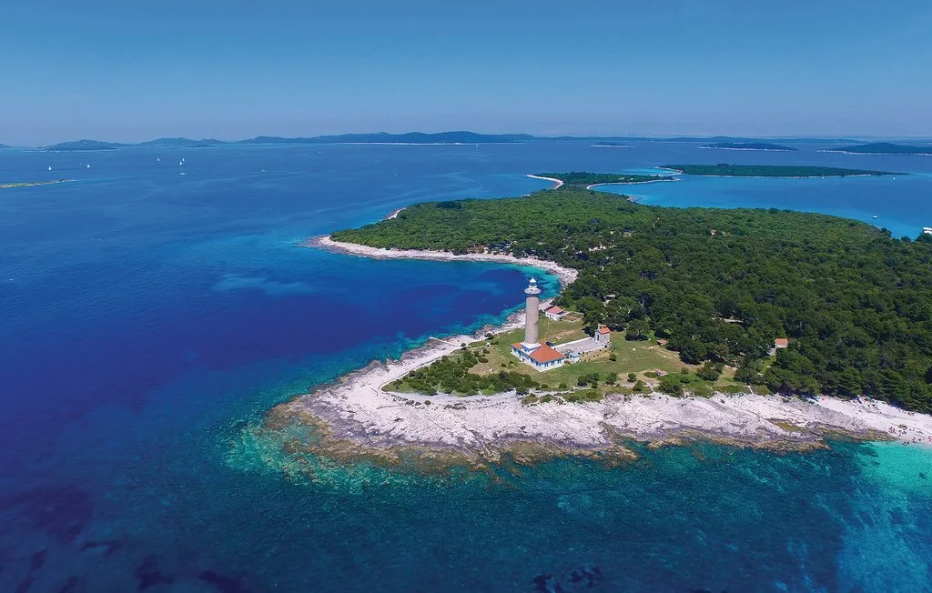 Vista aérea de un faro en una península boscosa rodeada de aguas azules.