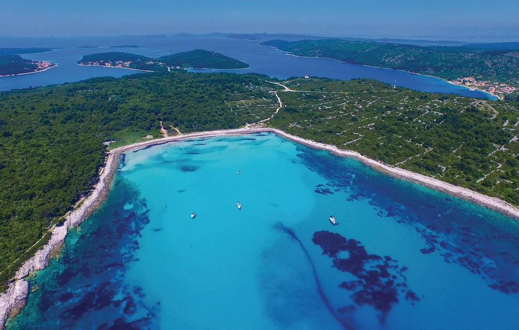 Vista aérea de una bahía turquesa rodeada de costa boscosa y barcos dispersos.