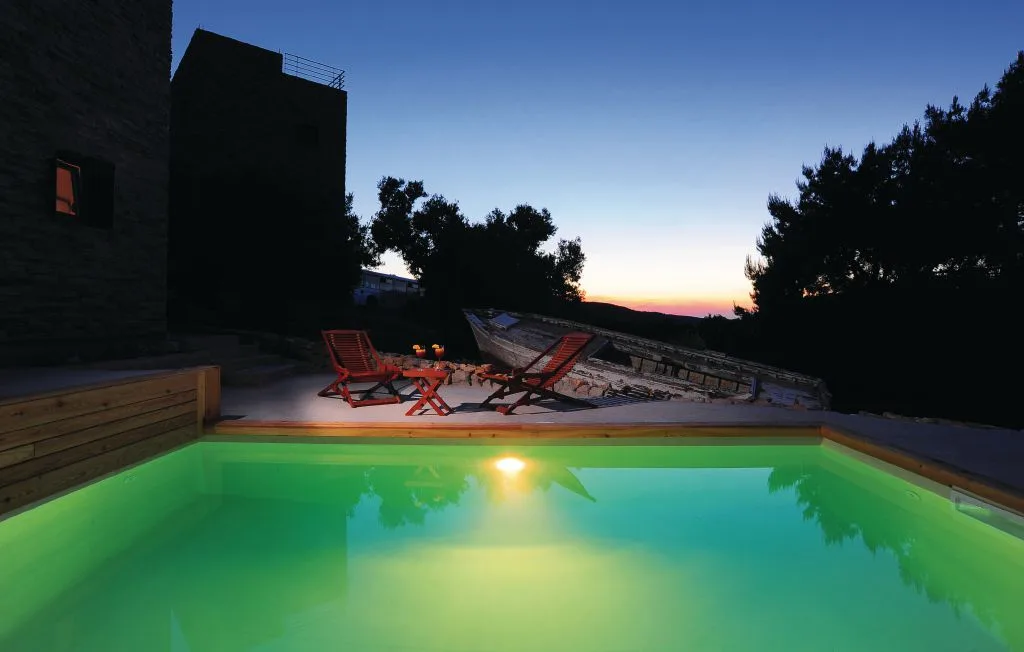 Una piscina exterior iluminada está junto a tumbonas al anochecer.