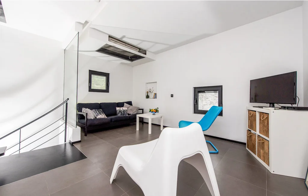 Una sala de estar moderna con un sofá oscuro, una silla blanca y un televisor en la pared.