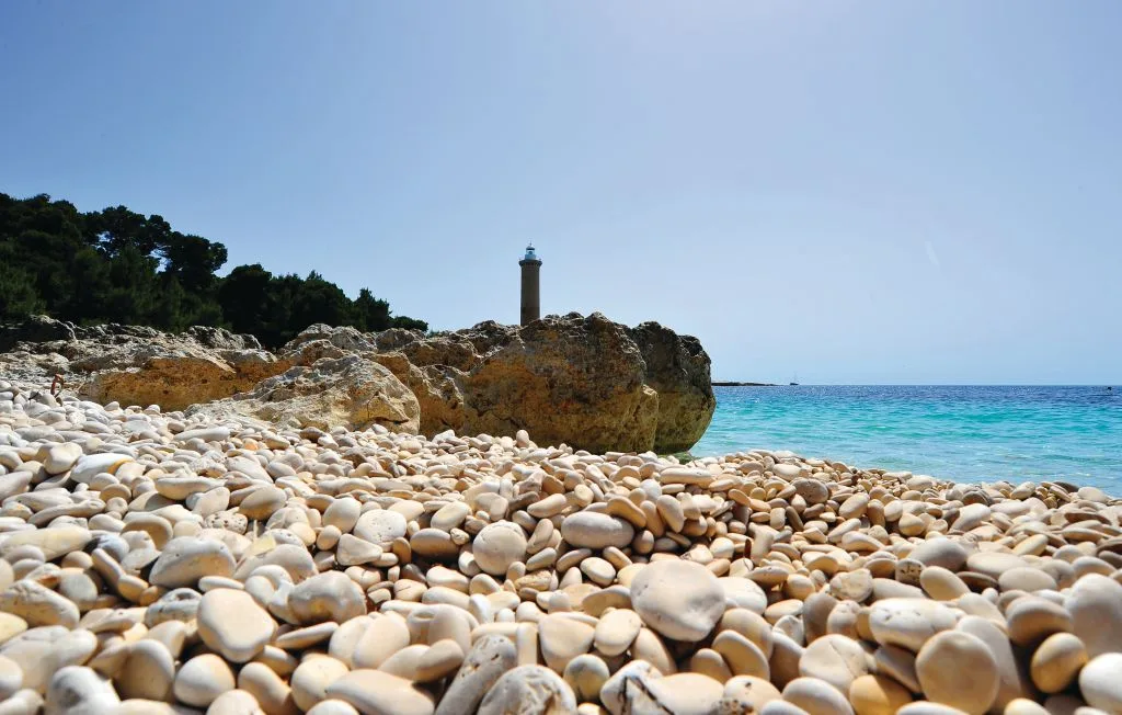 Una playa de guijarros junto a aguas turquesas, con afloramientos rocosos en la orilla.