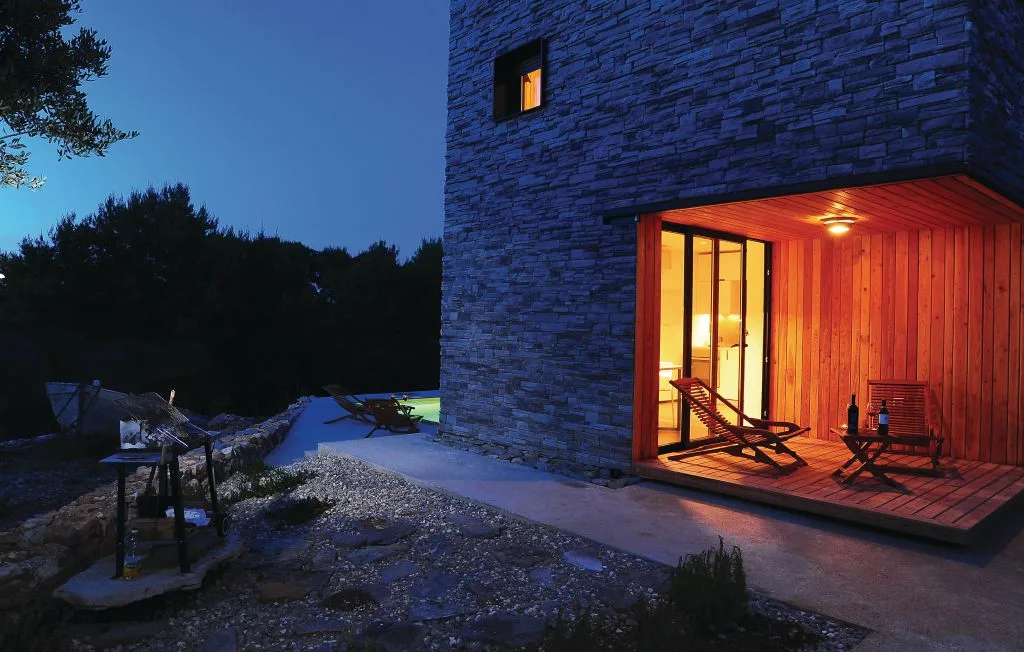 Una fachada de piedra da a un patio de madera iluminado y con asientos al anochecer.