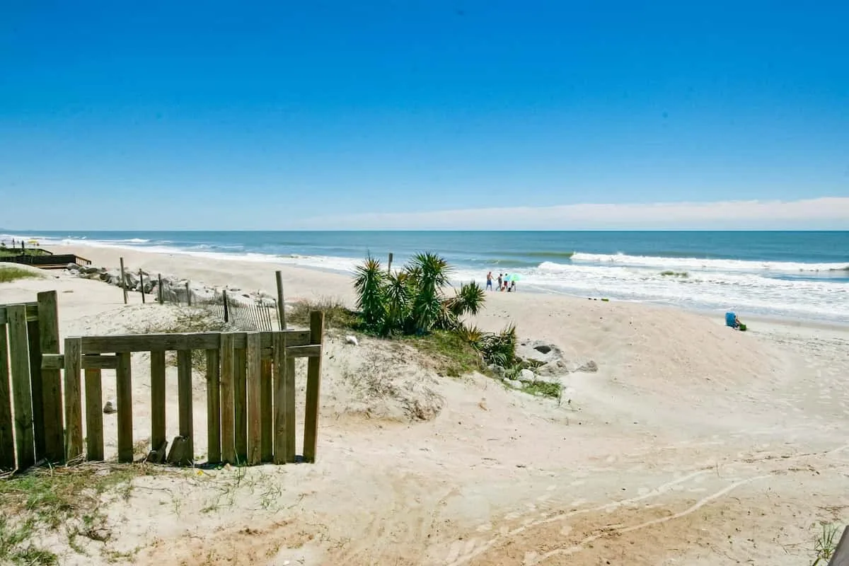 Una playa de arena se abre al océano bajo un cielo azul despejado.