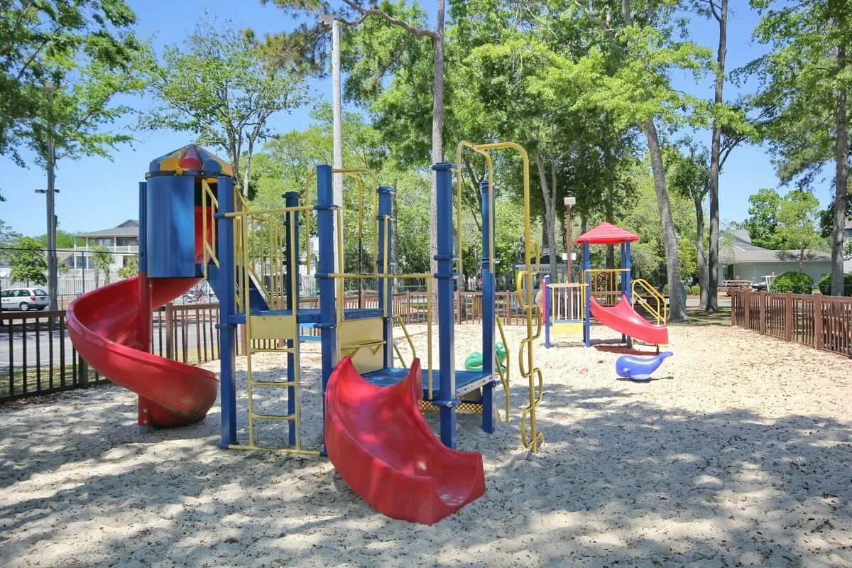 Un parque infantil al aire libre con toboganes coloridos y estructuras para trepar bajo árboles frondosos.