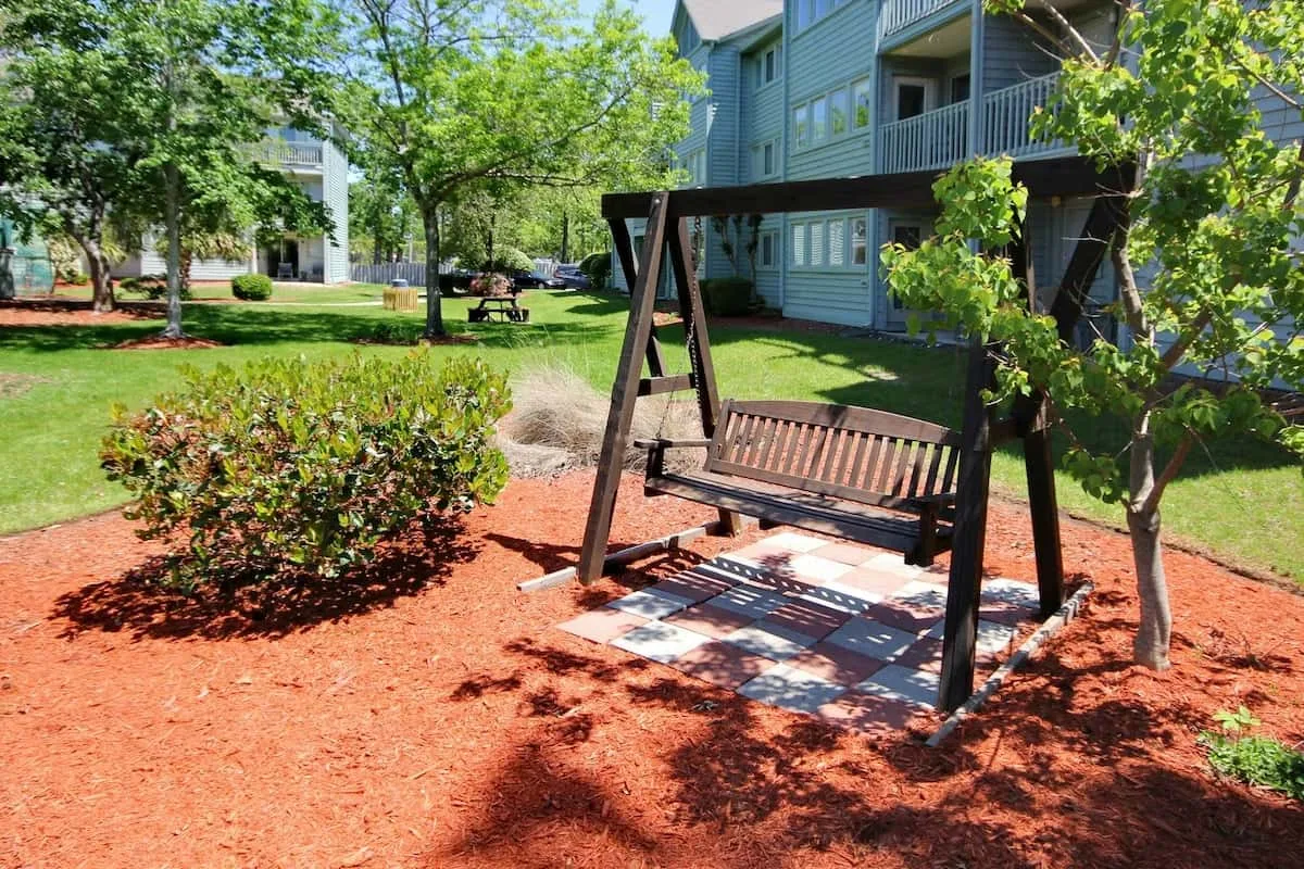 Un patio ajardinado con un columpio de madera bajo árboles frondosos.