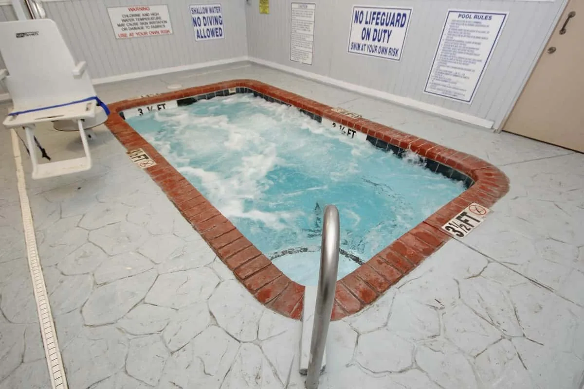 Un jacuzzi interior está en una sala con baldosas y una barandilla metálica.