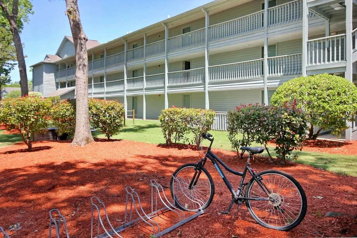 Un aparcamiento para bicicletas está junto a un patio ajardinado frente a un edificio de varias plantas.