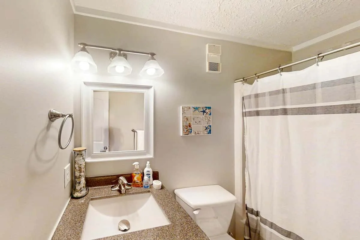 Un tocador de baño con lavabo y espejo junto a una cortina de ducha.