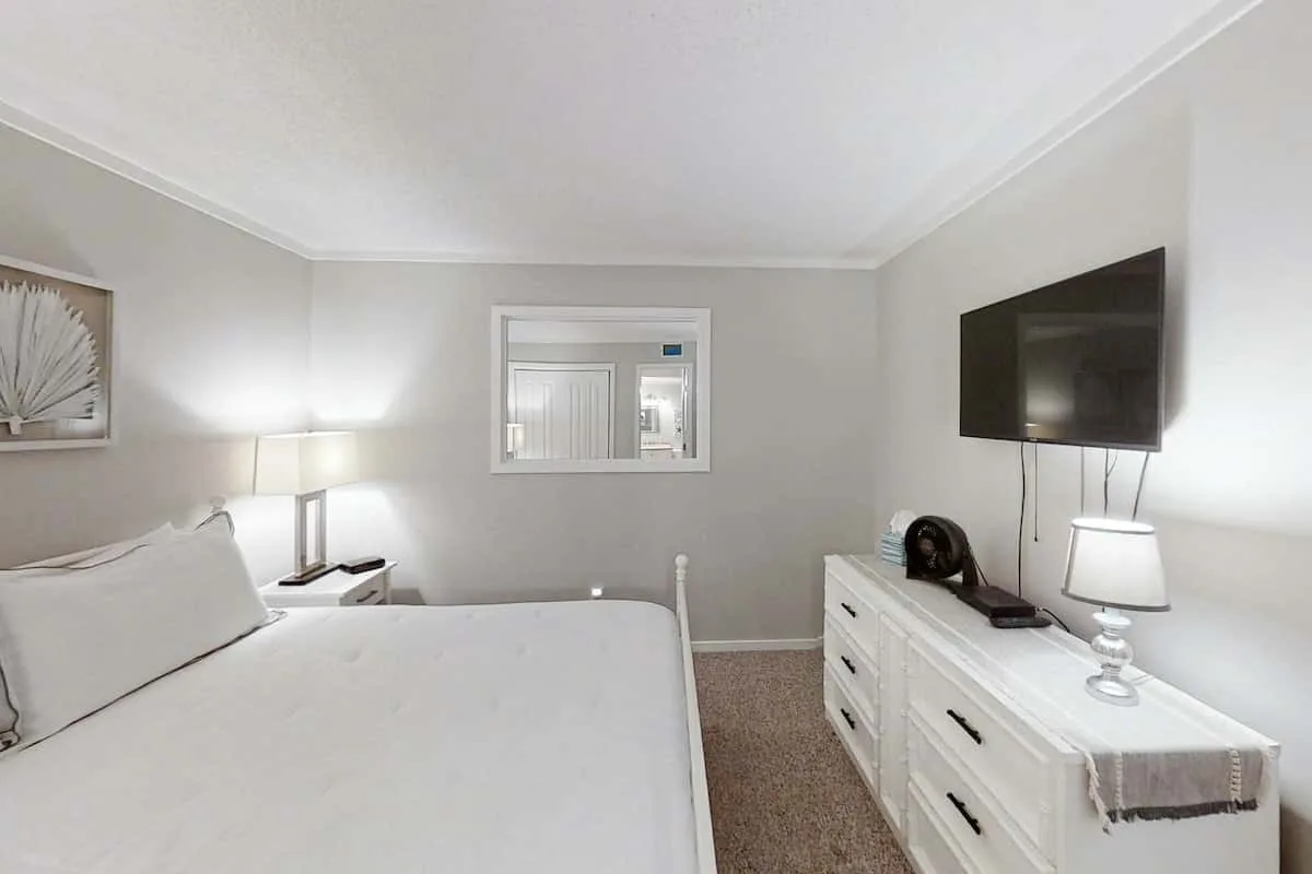 Un dormitorio con una cama, una cómoda y un televisor montado en la pared.