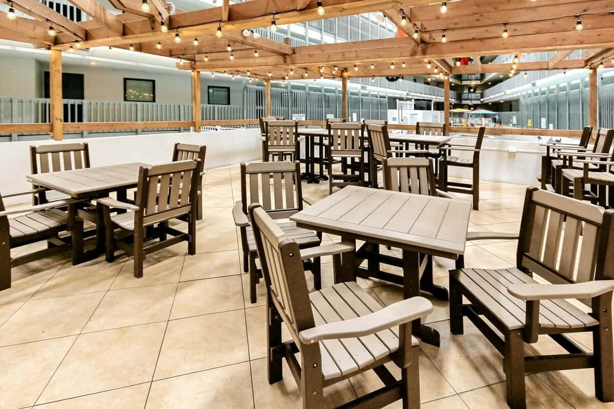 Una zona de comedor con mesas y asientos de madera bajo una pérgola.