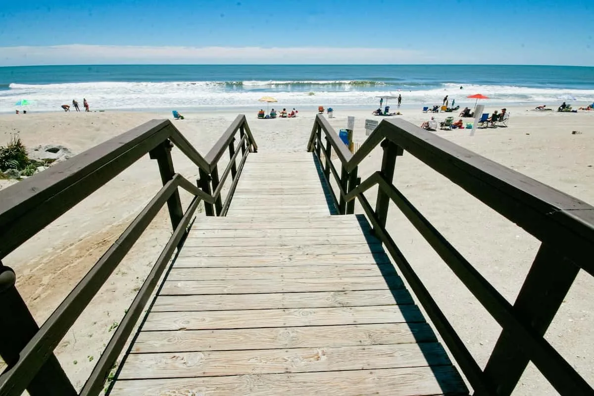 Una pasarela de madera atraviesa la playa de arena hacia el océano.