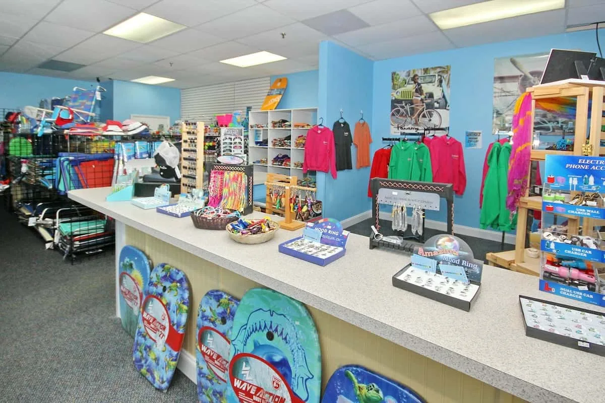 Un mostrador de tienda bien iluminado exhibe recuerdos, ropa y artículos de playa.