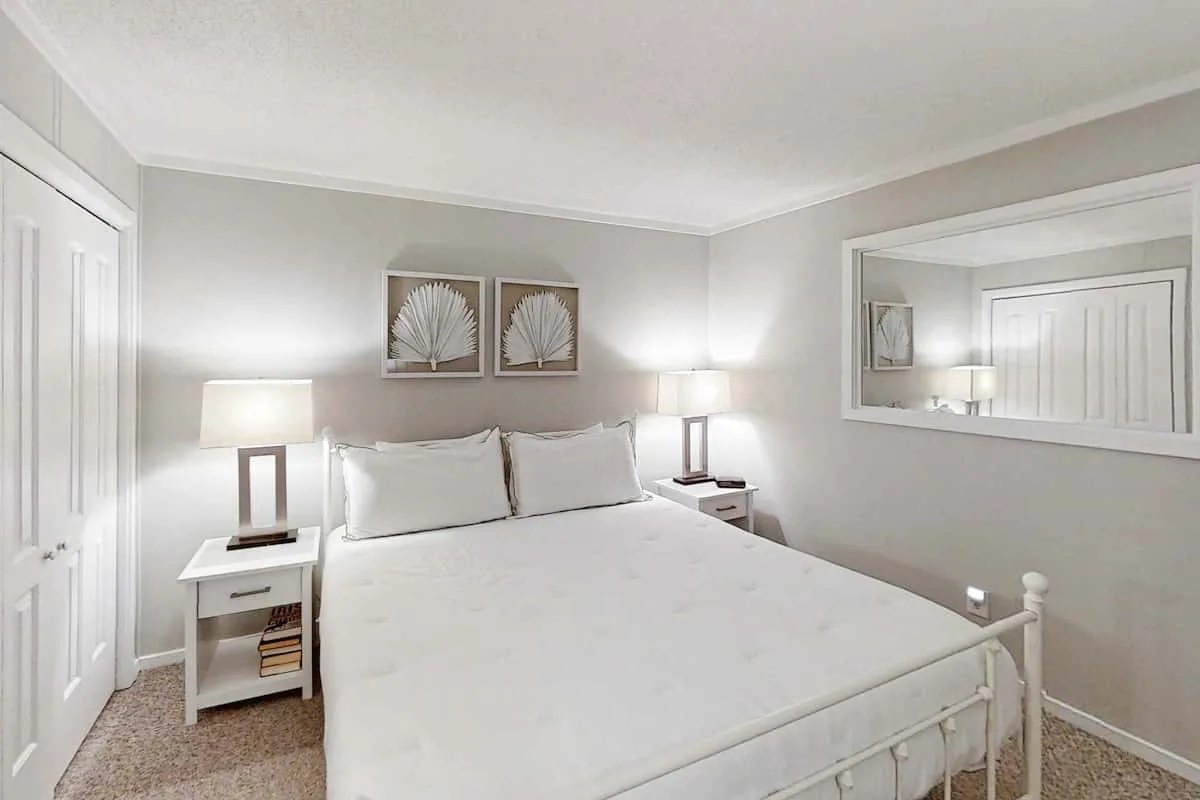 Un dormitorio con una cama blanca, mesitas de noche y un espejo grande en la pared.