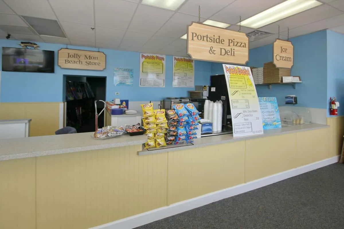 Un mostrador de refrigerios exhibe bolsas de papas fritas bajo letreros de pizza y helado.