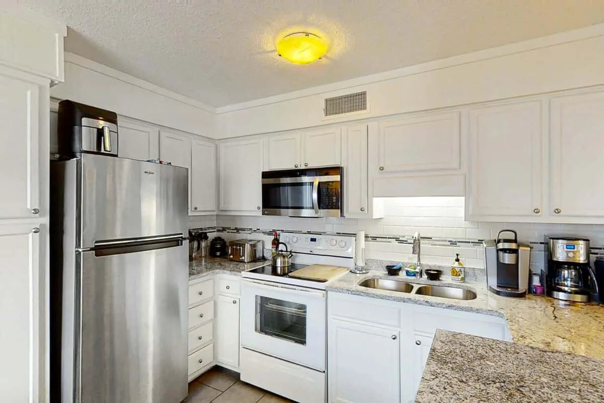 Una cocina luminosa con gabinetes blancos, electrodomésticos de acero inoxidable y una encimera de piedra.