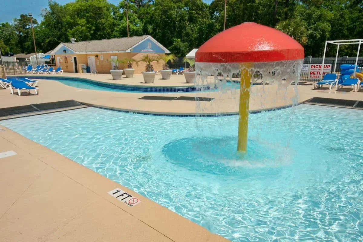 Una piscina al aire libre tiene una fuente con forma de hongo que rocía agua.