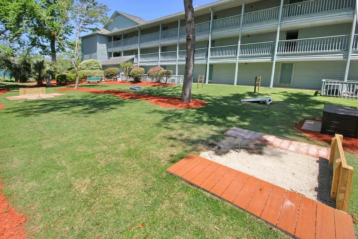 Área recreativa al aire libre con césped y una estructura de madera junto a un edificio largo.