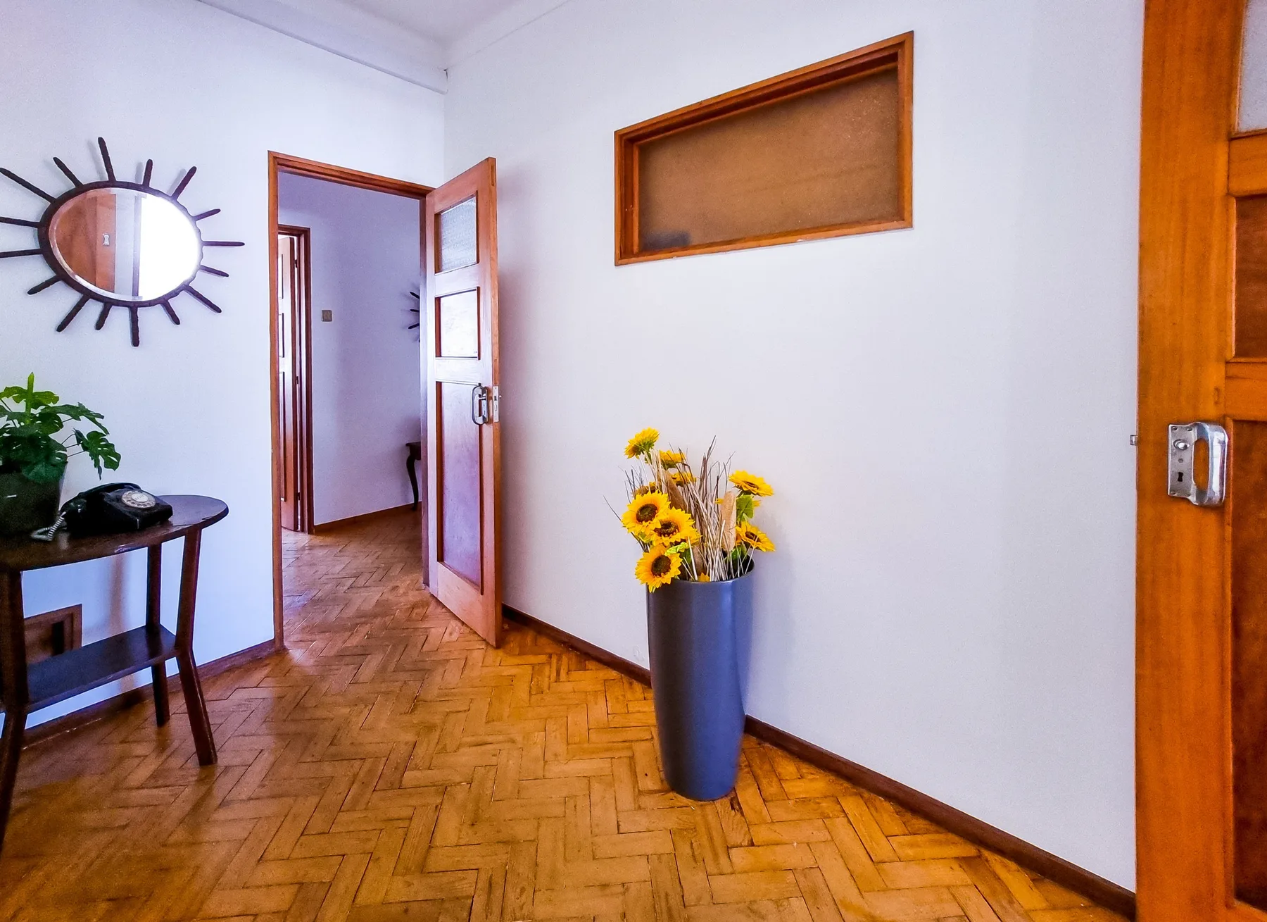 Un recibidor de apartamento con suelo de parquet y un jarrón de flores amarillas.